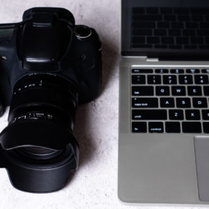A black digital camera and a computer laptop on a table.